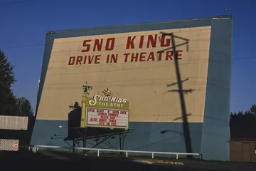 The big painted screen of the Sno-King Drive-in Theatre on Highway 99, against a deep blue sky.